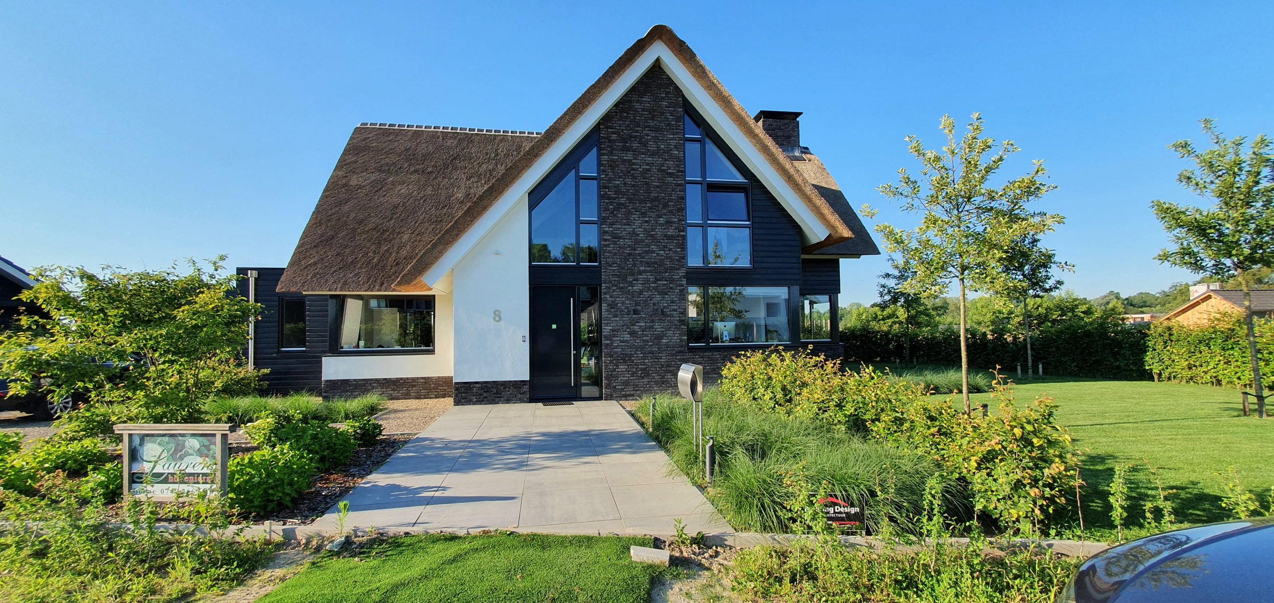 Moderne villa met rieten kap, grote ramen en groene tuin
