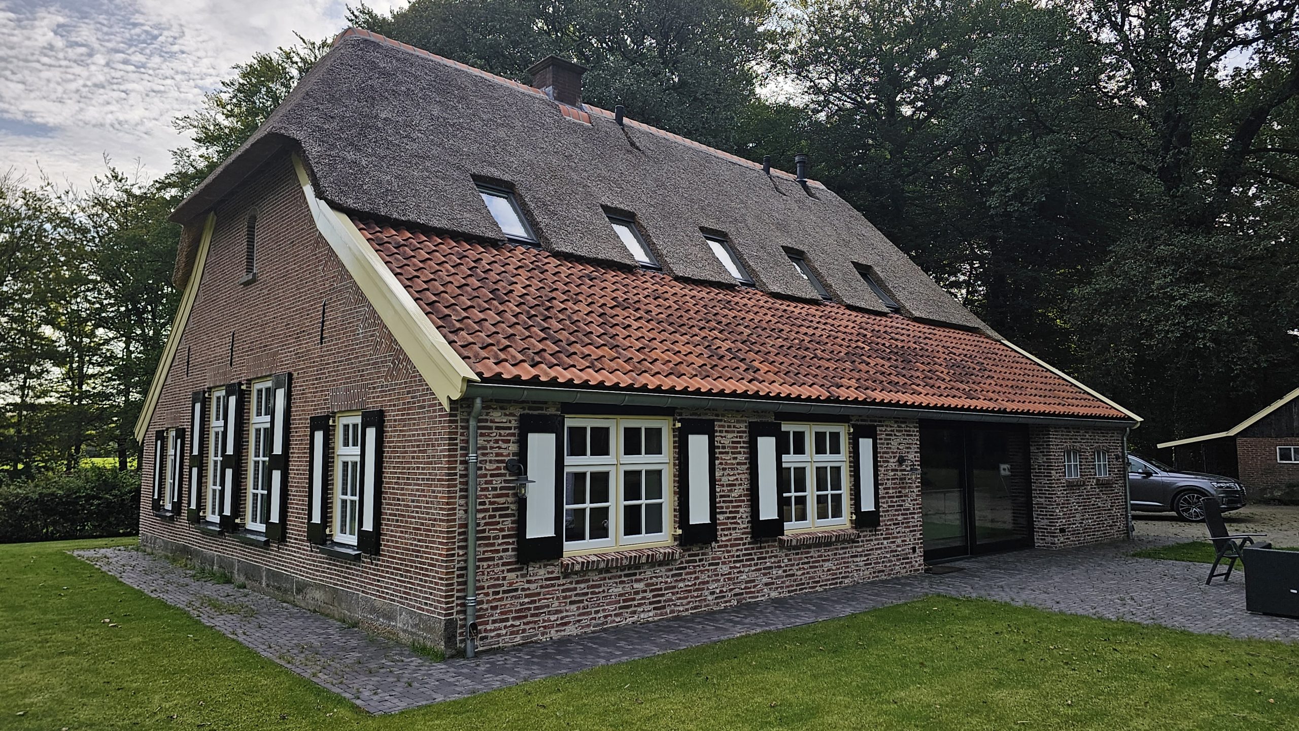 Bakstenen boerderij met rieten kap, rode pannen en luiken.