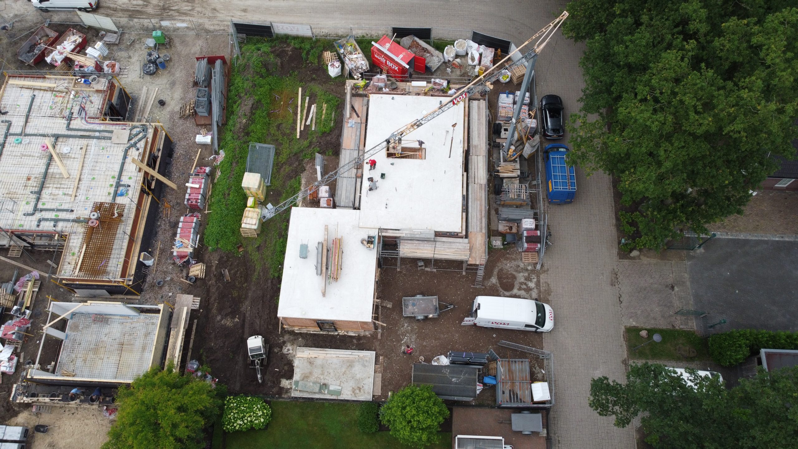 Luchtfoto van bouwplaats met kraan, woningen in aanbouw en bestelbus.