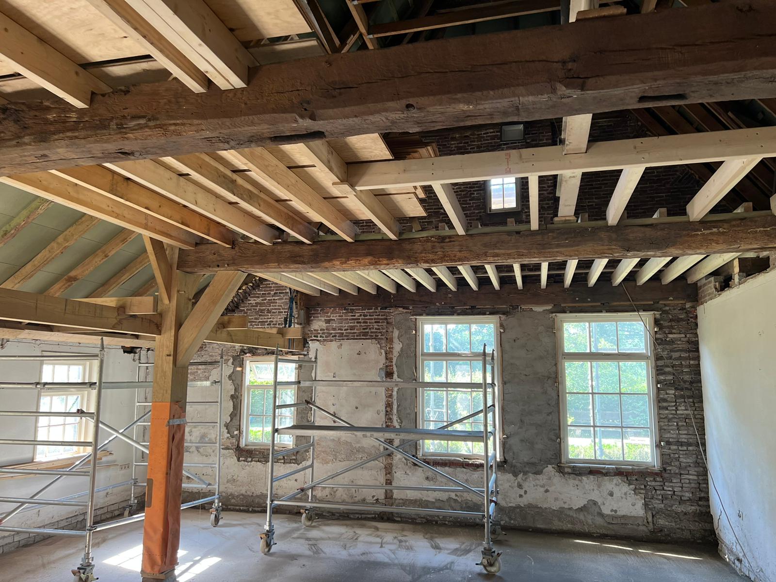 Renovatie van oud interieur met houten balken, steigers en grote ramen.